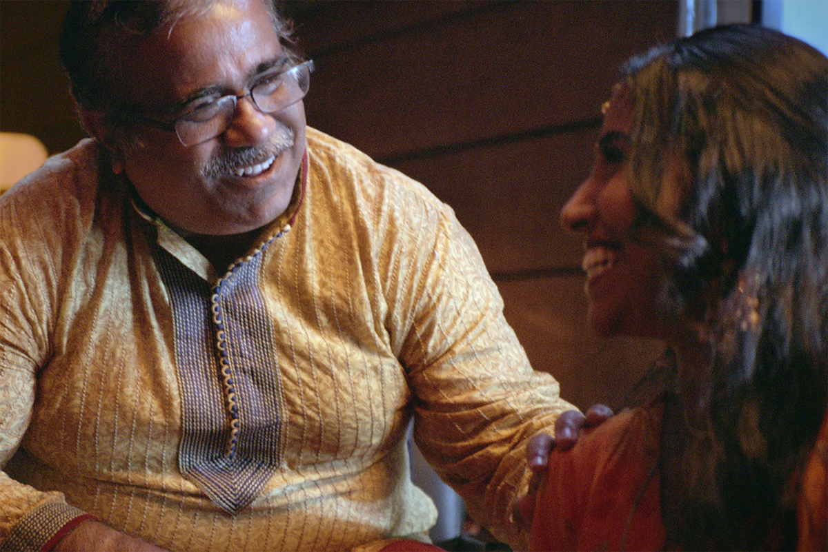 A man conversing with a woman with his hand on her shoulder, both smiling